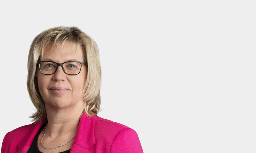 Jutta Riedmueller, Manager Rechnungswesen Portraetfoto von Jutta Riedmueller vor grauem Hintergrund
